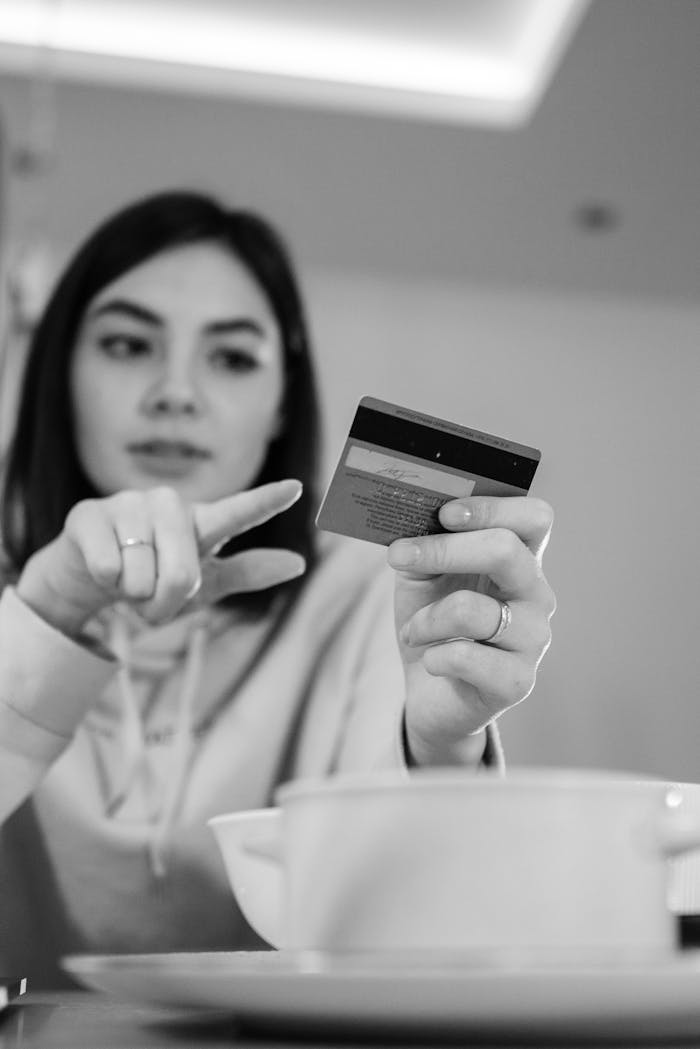 Black-and-white image of a woman pointing at a credit card indoors.